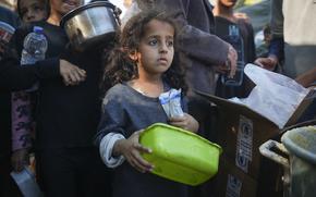 A Palestinian girl holds a container while standing in line for food handouts in Gaza.