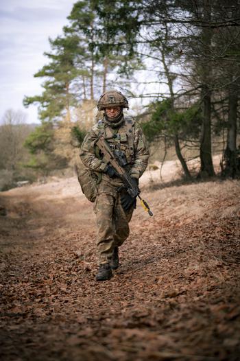 A British soldier in uniform walks along a dirt path holding a weapon.