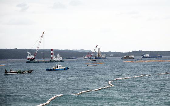 Construction vessels sit in open water with a coastline in the background.