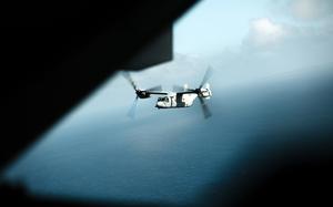 An Osprey air craft flies above water.