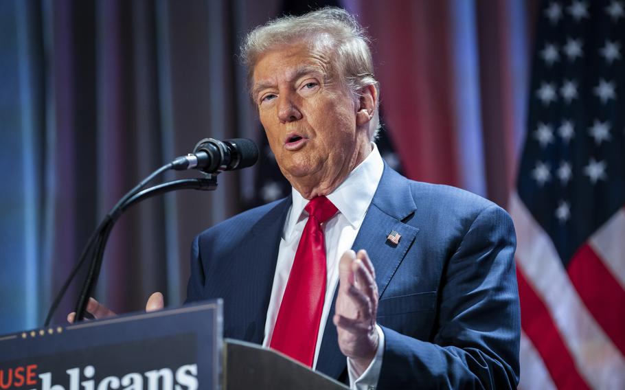 Donald Trump gestures with his hands as he stands at a podium in front of a U.S. flag and speaks into a microphone.