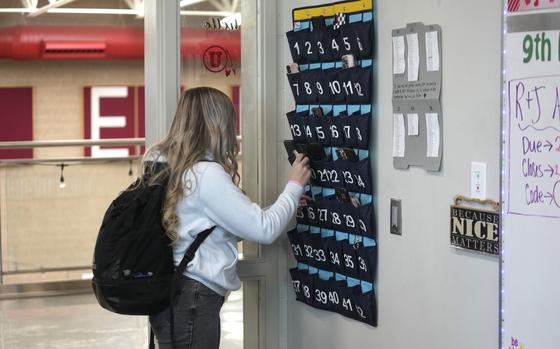 A ninth grader places her cellphone in to a phone holder as she enters class at Delta High School, Friday, Feb. 23, 2024, in Delta, Utah. At the rural Utah school, there is a strict policy requiring students to check their phones at the door when entering every class. Each classroom has a cellphone storage unit that looks like an over-the-door shoe bag with three dozen smartphone-sized slots. (AP Photo/Rick Bowmer)