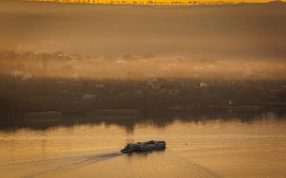 A ferry is seen from a distance on a river at sunset or sunrise.