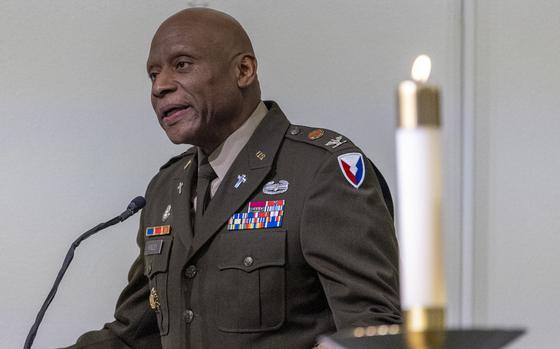 A man in uniform speaking at a podium with a white candle in the foreground to his left.