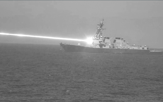 A black and white photo of a destroyer firing a beam of white light.