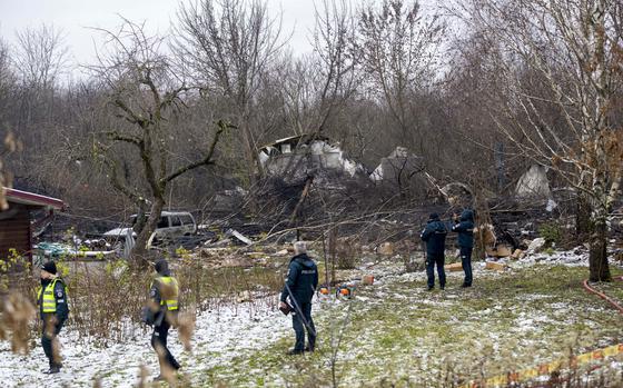 Emergency workers survey the site of a crashed plane resting among trees.