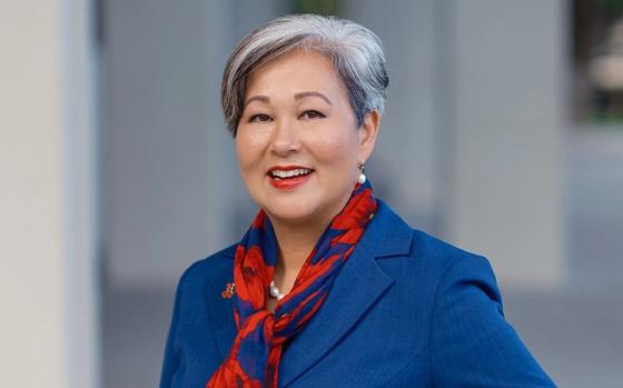 A woman with short, graying hair poses while wearing a blue blazer and red scarf.