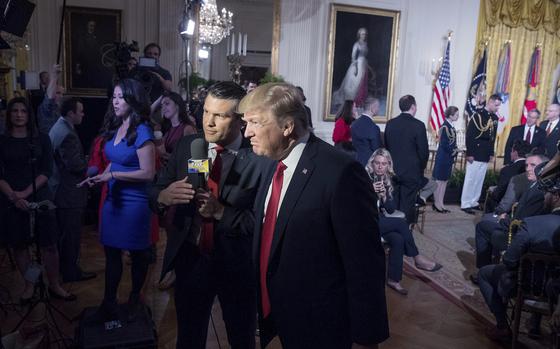 Pete Hegseth holds a microphone and speaks with Donald Trump at an event inside the White House.