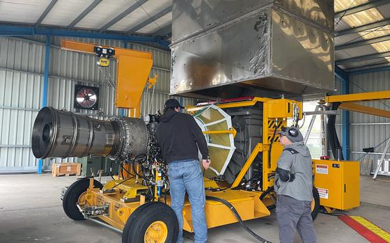 Two men stand near a digital engine diagnostic tool in a hangar.