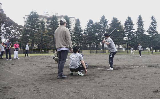 A Japan Air Self-Defense Force member is at bat with an catcher kneeling behind him. 