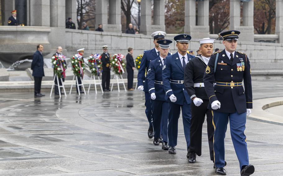 Service members in uniform march out after laying wreaths.