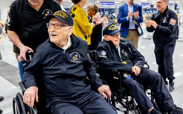 Two military veterans in wheelchairs are greeted at the airport.