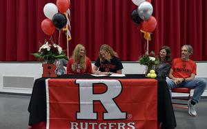 Stella Schmitz, center, signs her National Letter of Intent to play tennis for Rutgers University during a ceremony on Nov. 13, 2024, at Kaiserslautern High School. Left is Schmitz's mother, Clare Barnard-Schmitz, and right are Kaiserslautern tennis coaches Elizabeth and Gary Martin. Hidden behind the flowers at left is Stella's father, Frank Schmitz.