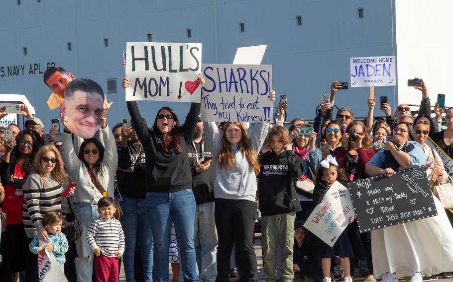 Family and loved ones hold signs during a homecoming ceremony for the USS Stockdale