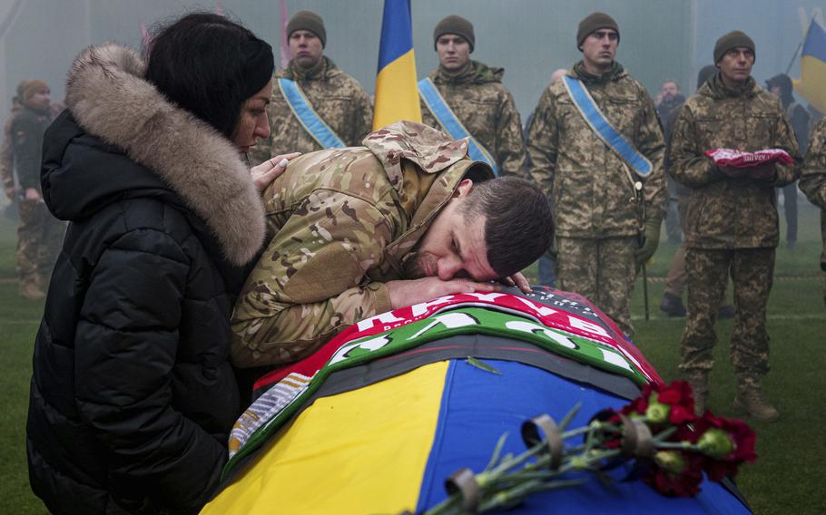 A Ukrainian service member rests his head on the yellow-and-blue coffin of his comrade.