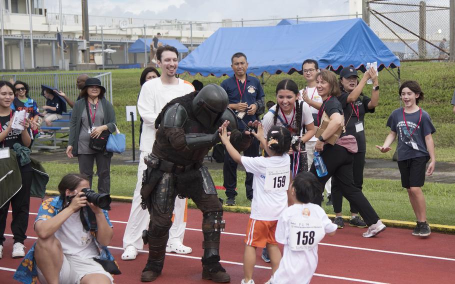 A person dressed as the Mandalorian from Star Wars gives high-fives to child athletes on a track.