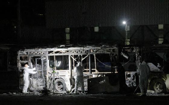 The skeleton of a bus is examined at night by investigators in white protective suits.