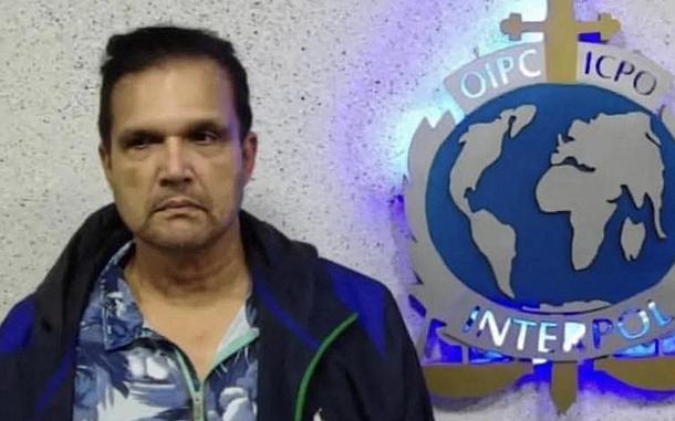 A man stands for a mugshot next to the emblem for Interpol Venezuela.