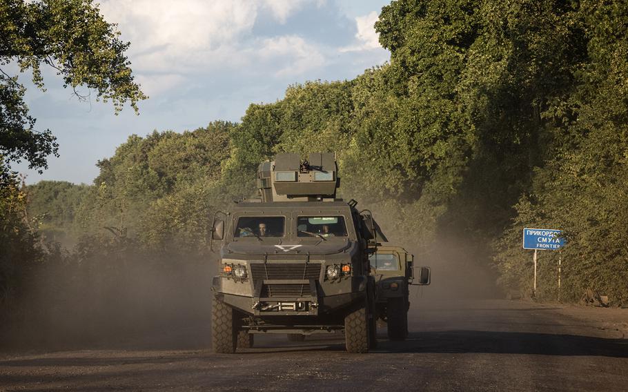 Military vehicles drive down a road near a sign indicating that the border to Russia is approaching north of Sumy, Ukraine, on Thursday.