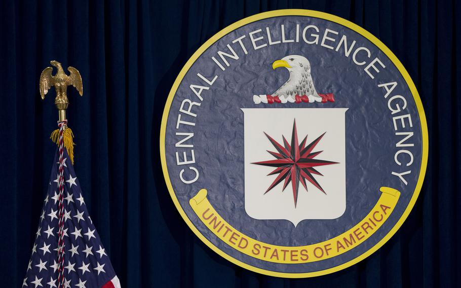 The seal of the CIA on a black background next to the American flag.