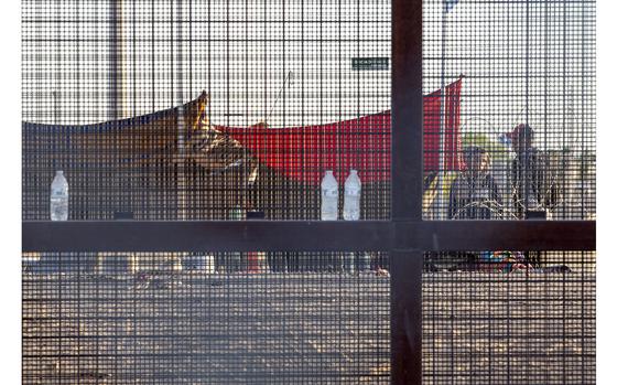 FILE - Two migrants, part of a small group, are seeing through the mesh ...