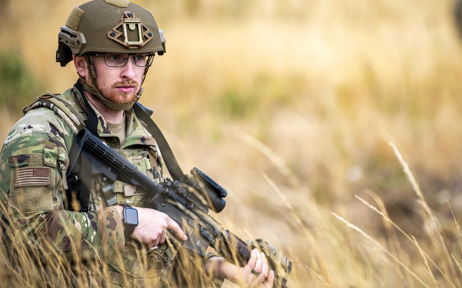 A bearded airman holds a firearm. 