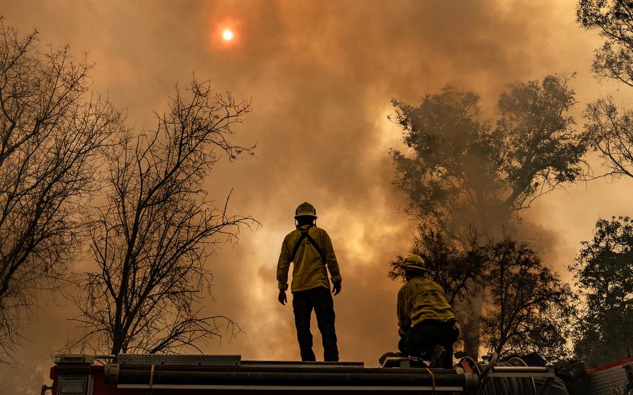 Firefighters stand on top of a fire truck.