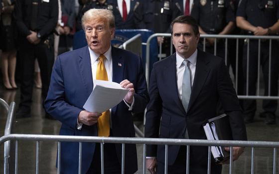 Donald Trump speaks while standing next to his lawyer in front of a metal barrier.