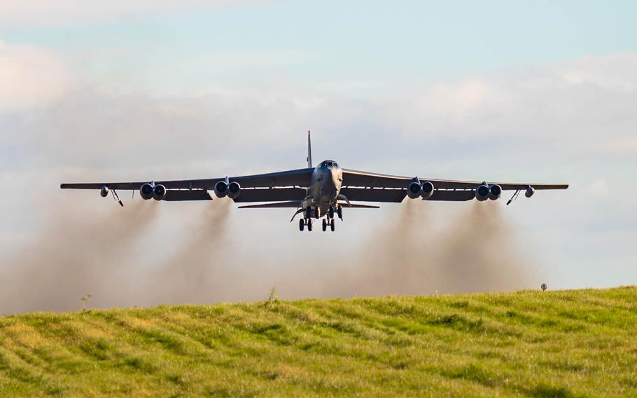 A B-52H Stratofortress flies over a field in England with exhaust trailing behind it.