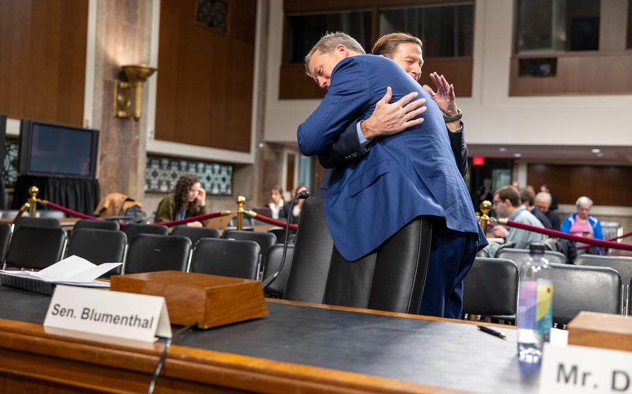 Two men hugging in front of a row of empty seats.