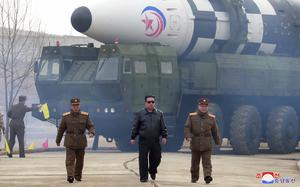 Kim Jong Un, wearing a black leather jacket and sunglasses, walks with two military officials walk in front of a ballistic missile.