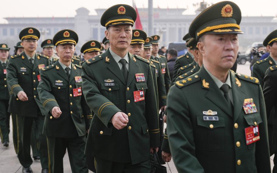 Chinese military officials in green dress uniforms march in formation through a city square.