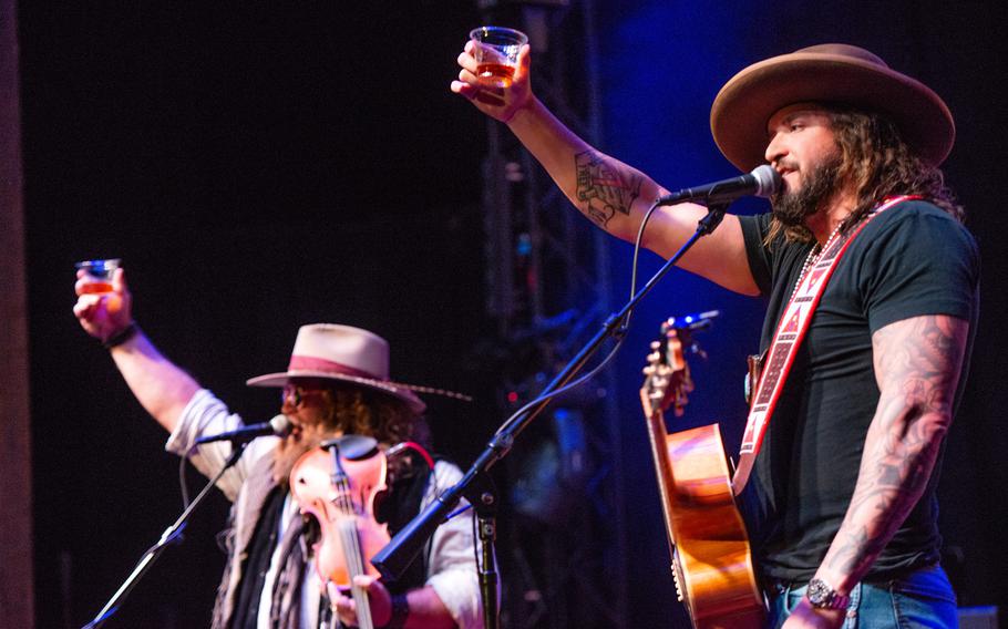 The country music duo War Hippies — Marine veteran and guitarist Scooter Brown and Army veteran and violinist Donnie Reis — toast the crowd during a performance on March 9, 2023, at MadLife Stage & Studios in Woodstock, Ga., just north of Atlanta.