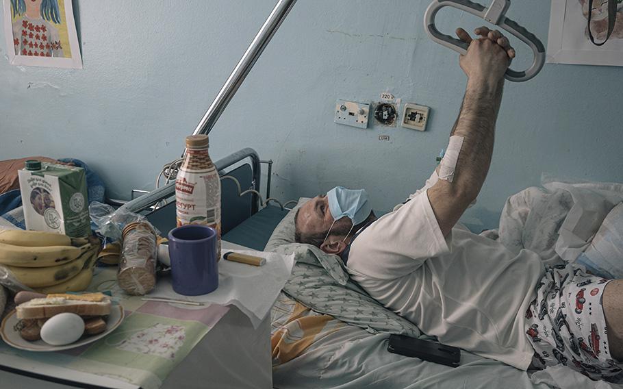 Ukrainian serviceman Mykhailo, 34, lies on a bed while Oksana, a nurse, and Vadym, a traumatologist, change his bandages. 