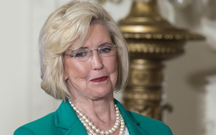 Lilly Ledbetter, wearing glasses and a green blazer, smiles as she looks off to the side.