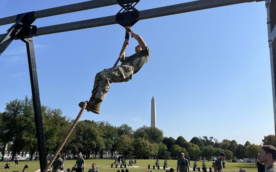 A soldier climbs a rope during the Army Best Squad Fitness Event in Washington, D.C., with the Washington monument visible in the background, Oct. 12, 2024.