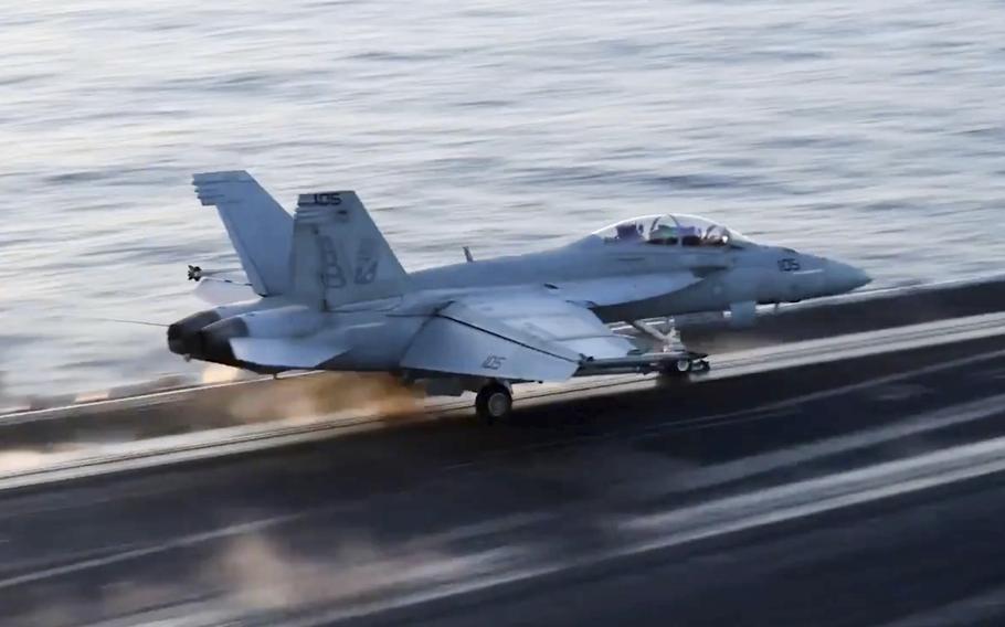 A military fighter jet speeds down the runway of an aircraft carrier to take off.