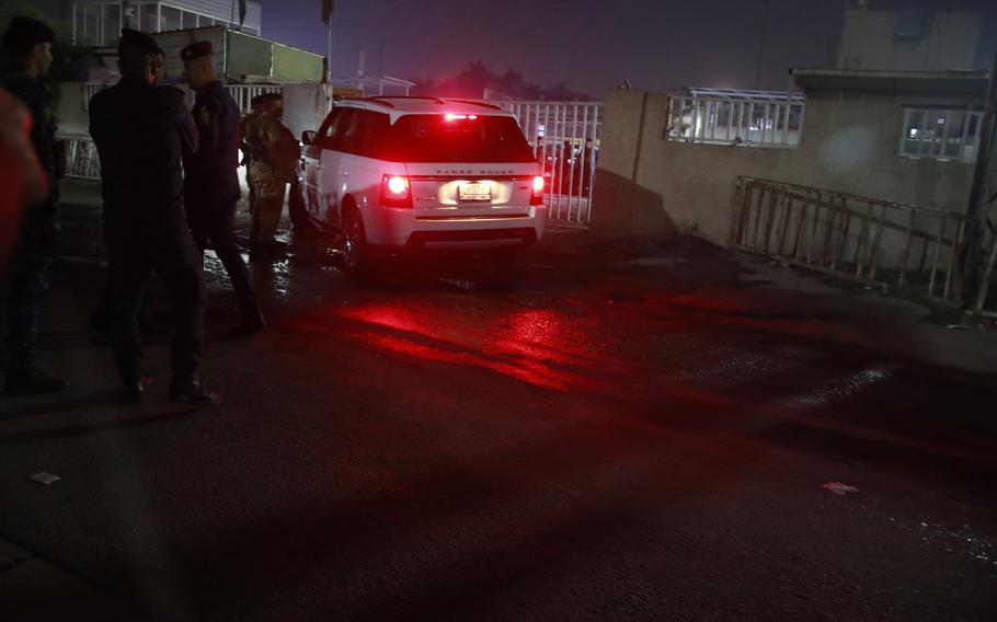 A car and shadowed security personnel are seen at night.