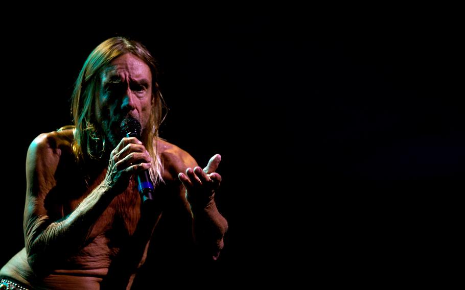 A shirtless Iggy Pop gestures to the audience.