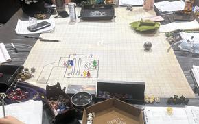 A Dungeons and Dragons playing board sits on a table surrounded by dice, paper and notebooks.