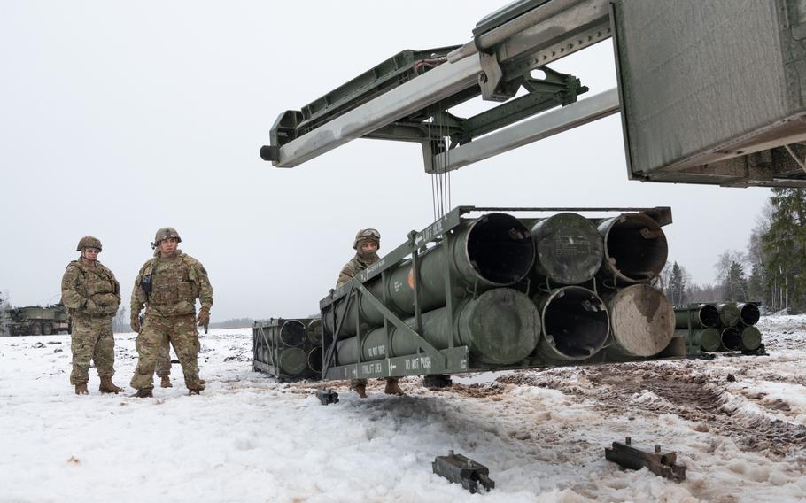 Members of the U.S. Army-led Task Force Voit work in the snow to load a High Mobility Artillery Rocket System with test rockets.