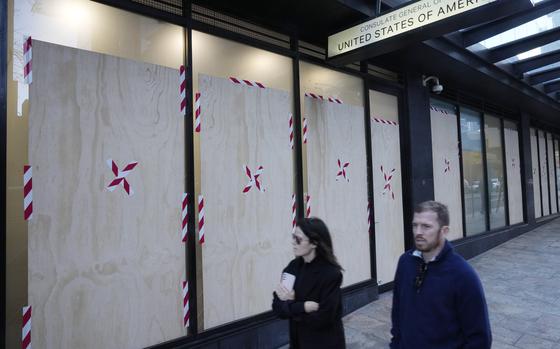 A couple walks past the boarded windows at the U.S. consulate as police investigate the vandalism in Sydney, Monday, June 10, 2024. A suspect is believed to have smashed nine holes in the reinforced glass windows of the building in North Sydney after 3 a.m., a police statement said.