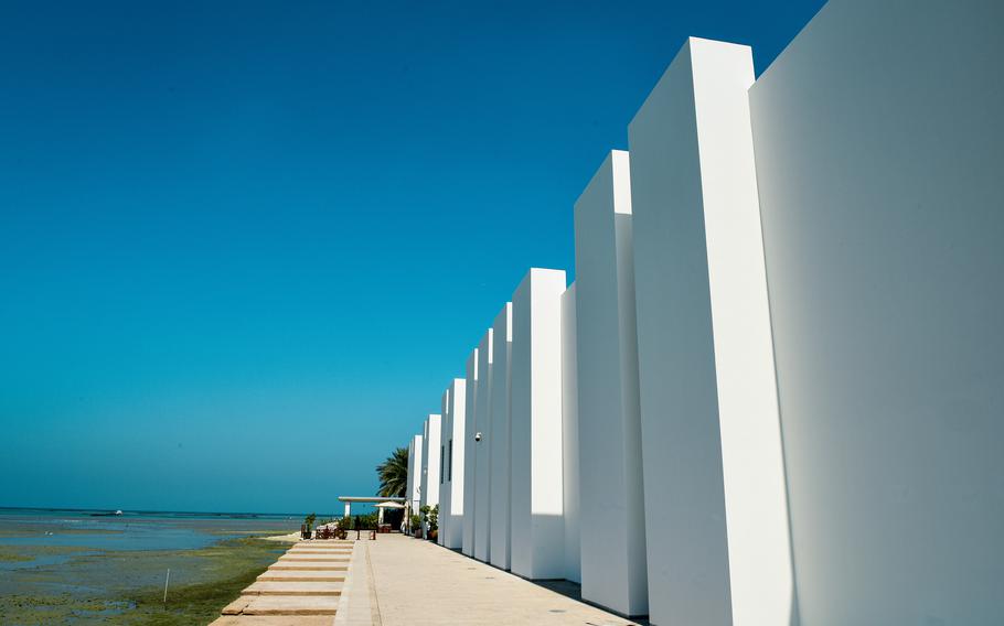 The tall white outside wall of the Qal’at al-Bahrain museum is seen on the right, next to the water’s edge. The museum showcases archaeological findings of the Bahrain Fort.