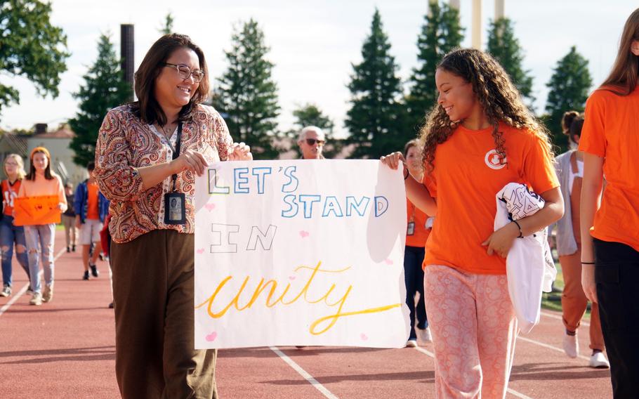 A woman and a girl walking on a track each hold one end of a poster that reads 'Let's Stand in Unity'.