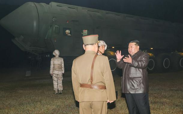 North Korean leader Kim Jong Un speaks to military leaders with a ballistic missile in the background.