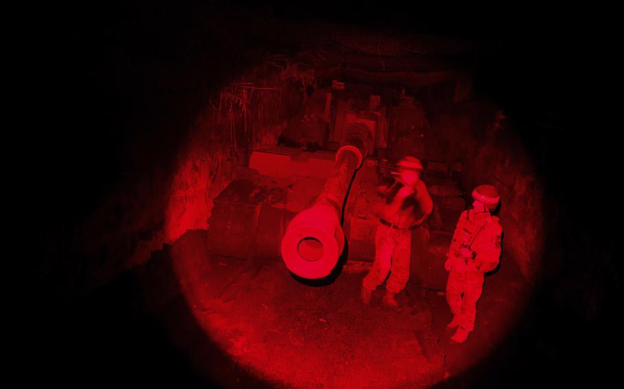 An infrared image of two soldiers in front of a tank.