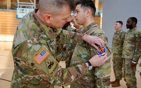 Col. Troy Danderson, commander of U.S. Army Garrison Wiesbaden in Germany, swaps out a patch on a soldier's uniform at Clay Kaserne in Wiesbaden on Feb. 19, 2025. The patch reflects the soldier's new alignment with the 56th Artillery Command.