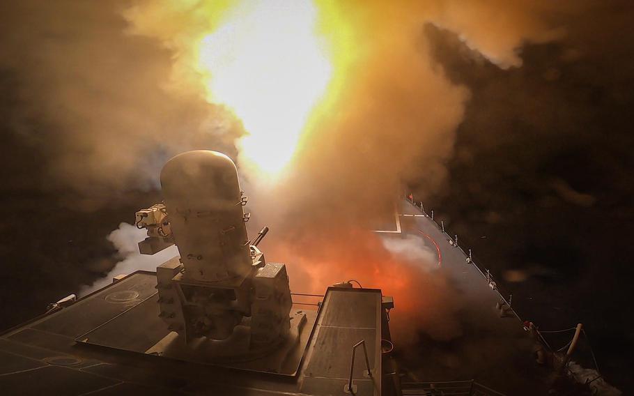 A flame illuminates the night sky as an artillery battery fires from aboard a U.S. destroyer.