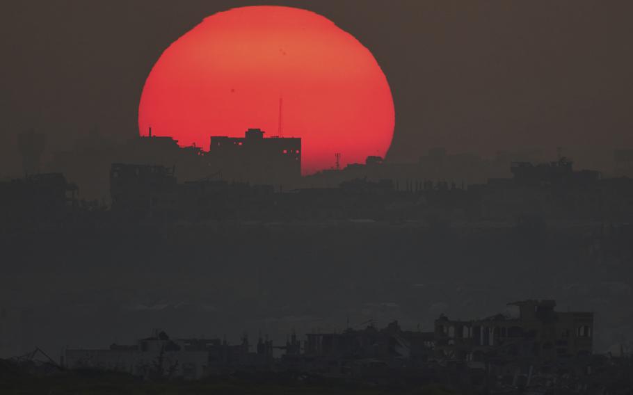 A red and setting sun makes a silhouette of a damaged skyline.