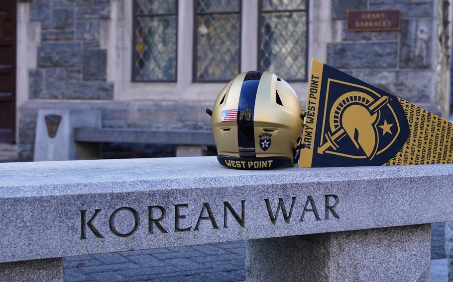 A black and gold West Point football helmet sits atop a Korean War memorial bench.